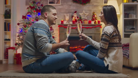 Couple-clinking-a-glass-of-champagne-sitting-on-the-carpet