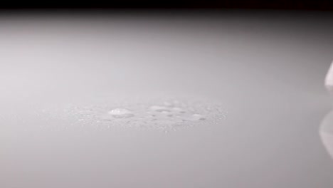 disinfectant spray being sprayed on a white reflective surface and being wiped down with a cloth