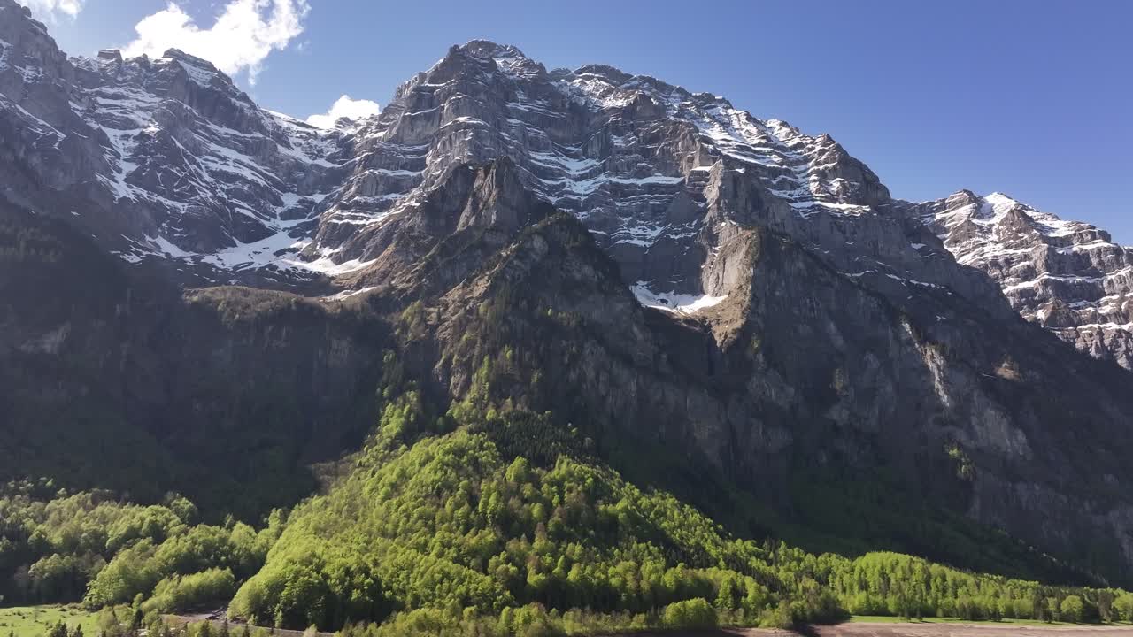 Drone advancing toward Klöntalersee, revealing snow-capped peaks and lush forests in Glarus, Switzerland