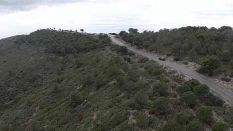 Road-trip,-a-car-driving-an-empty-hillside-road-in-wilderness