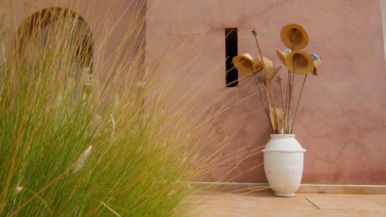 Close-up of straw hats hanging from bamboo sticks in a beautiful Moroccan vase, set against classic geometric architecture in Marrakesh, Morocco