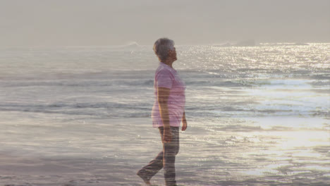 Animation-of-glowing-light-over-happy-senior-woman-walking-by-seaside