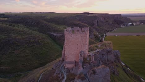 drone shot of the medieval oreja castle perched on a hilltop at golden hour near aranjuez, spain. scenic sunset over rural fields and rocky landscape.