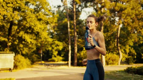 Una-Deportista-Con-Uniforme-Deportivo-De-Verano-Corre-En-El-Parque-Matutino-Y-Se-Echa-Agua-Encima-De-Una-Botella-Negra