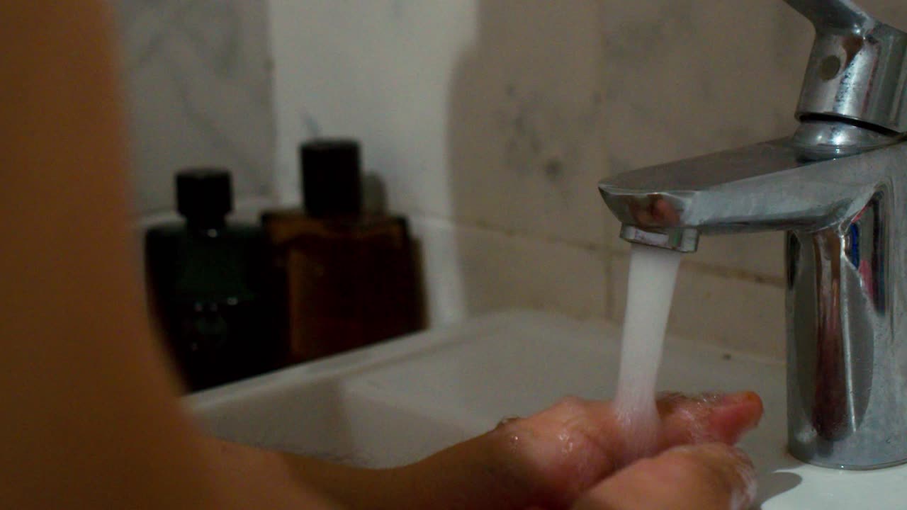 Young man's hand is turning a tap in a bathroom