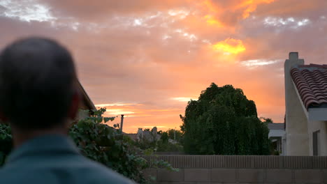 a middle aged man stares in awe at a colorful orange sunset from his suburban home backyard in los angeles, california