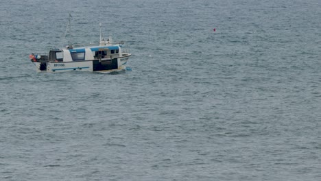 a small fishing vessel moves steadily across the gray sea under overcast skies near edinburgh, scotland. static wide shot with natural daylight