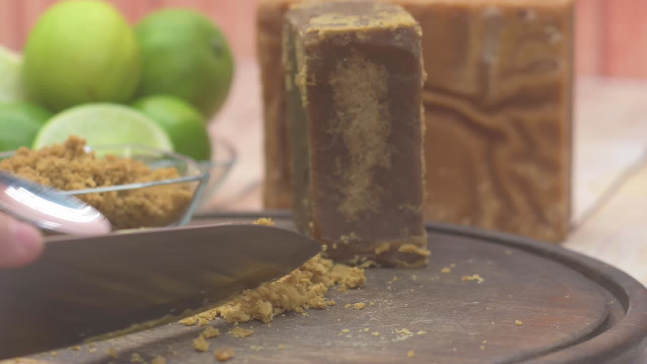 Inserimento statico che mostra in dettaglio la preparazione della limonata di canna da zucchero, con un coltello e un cucchiaio coperti di zucchero grezzo granulare (panela) accanto agli ingredienti essenziali del lime