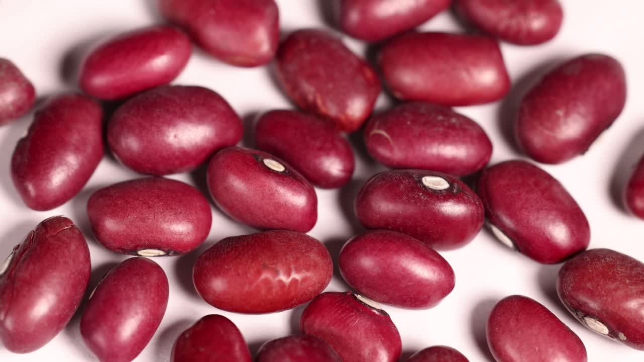 Close-up video of red bean seeds moving slightly on a white surface under bright lighting