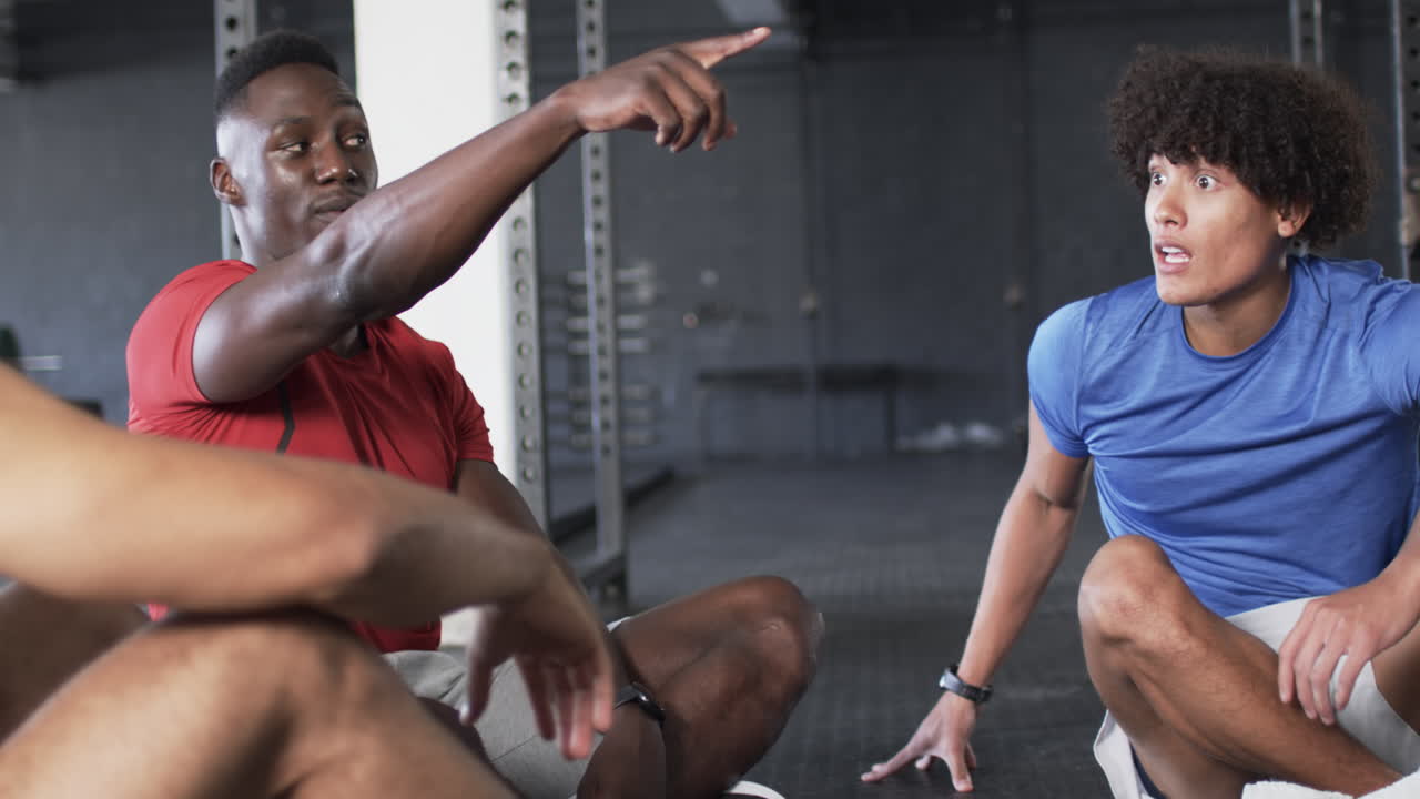 Discussing workout routine, men sitting on gym floor, focusing on fitness goals