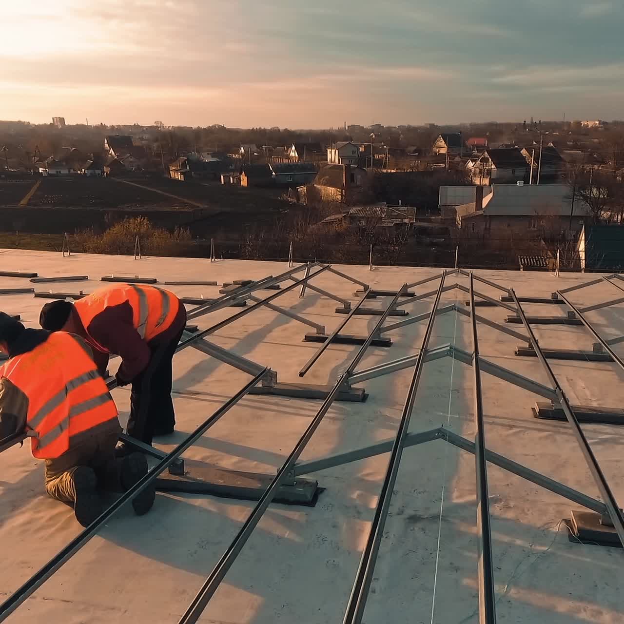 Preparative process for solar energy farm on a building. Workers install metal constructions on roof at sunset. Motion camera around.