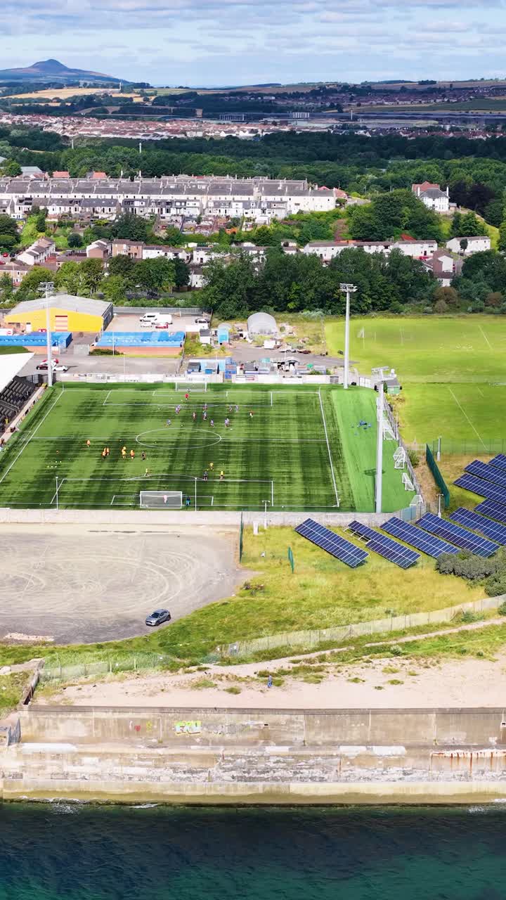 Un drone sorvola uno stadio di calcio, pannelli solari e campi di allenamento in pieno giorno, Dundee, Scozia