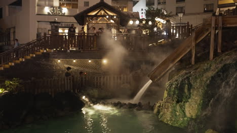 turistas reuniéndose y tomando fotografías del simbólico campo de agua caliente de kusatsu onsen en gunma por la noche después de encenderse con agua caliente humeante que sale