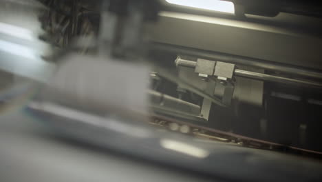 Close-up-of-a-printing-production-line,-parts-of-the-machine-moving,-paper-moving-forward-on-the-production