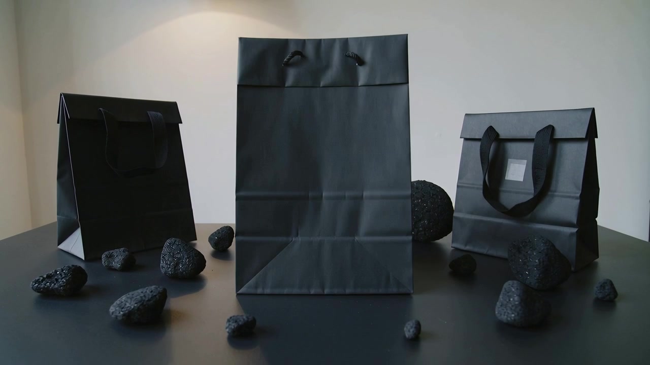 Tilting black center bag rising upright on table under overhead lamp, with pumice stones, side bags