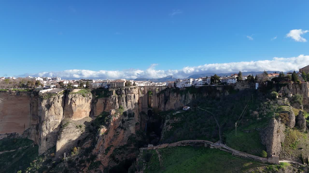 Aerial view of Ronda, Spain, highlighting the iconic Puente Nuevo bridge over the stunning El Tajo gorge, framed by white houses and a clear blue sky