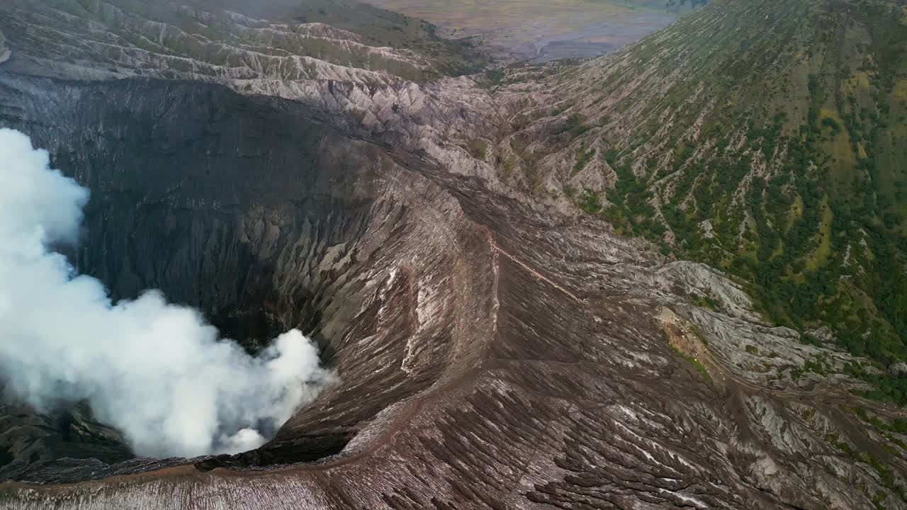 Filmato di un drone che riprende il vulcano Monte Bromo a Giava, con un cratere fumante, ripide pareti vulcaniche, formazioni rocciose a vista e ampi paesaggi di caldera modellati dall'attività vulcanica