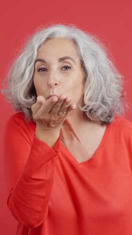 mature woman blowing a kiss on a red background