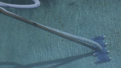 automatic pool cleaner operating underwater, efficiently removing dirt, debris, and leaves from the pool bottom, surrounded by clear water and vibrant blue tiles
