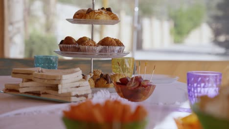 table with sweets for a party in summer, with a tray with croissants, sandwich, crudités, coloured glasses and white tablecloth