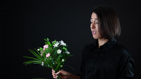 perfil de mujer joven mordiendo flor de ramo con expresión de cara repugnante, cámara lenta, toma de estudio, fondo negro