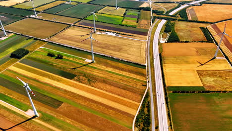 Beautiful colorful fields in the countryside with installed wind turbines. Cars ride by the highways crossing the landscape. Aerial view