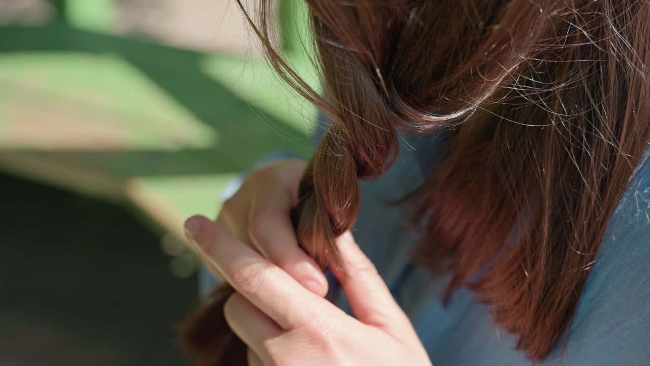 햇빛 아래 야외에서 땋은 머리를 만드는 백인 여성, 햇빛 아래에서 머리를 땋는 여성의 클로즈업, 자연 햇빛 아래 야외에서 머리카락을 땋는 하얀 피부를 가진 여성의 상세한 모습