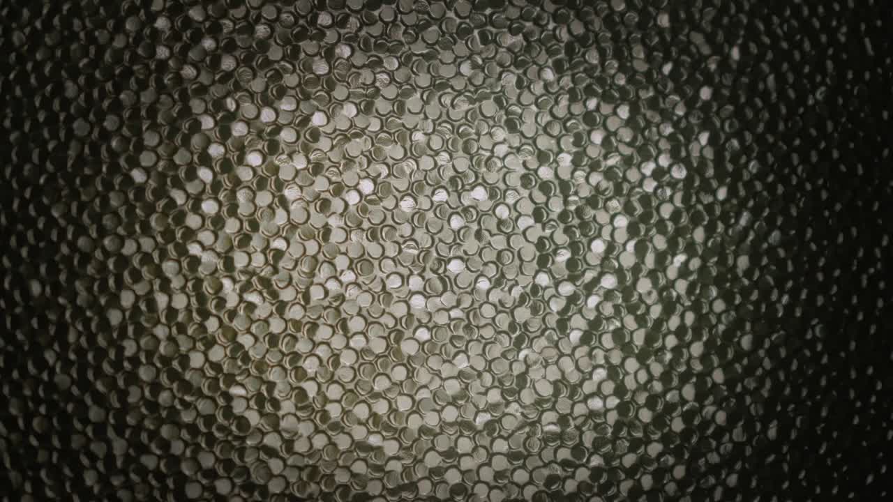 Water runs down dark textured mosaic glass with moody light background