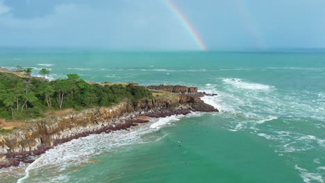 toma de drones de grandes olas cortando los acantilados con un arco iris en el fondo