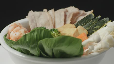 close up of a bowl of shabu ingredients spinning around on white table in the black background kitchen