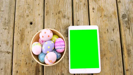 painted easter eggs in a bowl and digital tablet on wooden surface