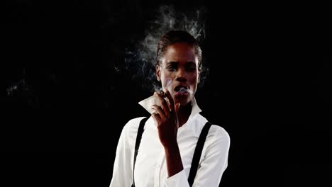 androgynous man smoking cigar against black background
