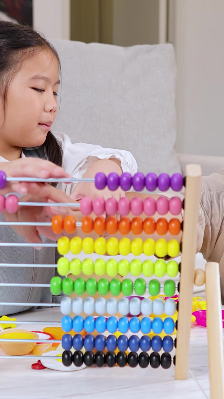 Asian father teaching daughter math using a colorful abacus in a bright living room.