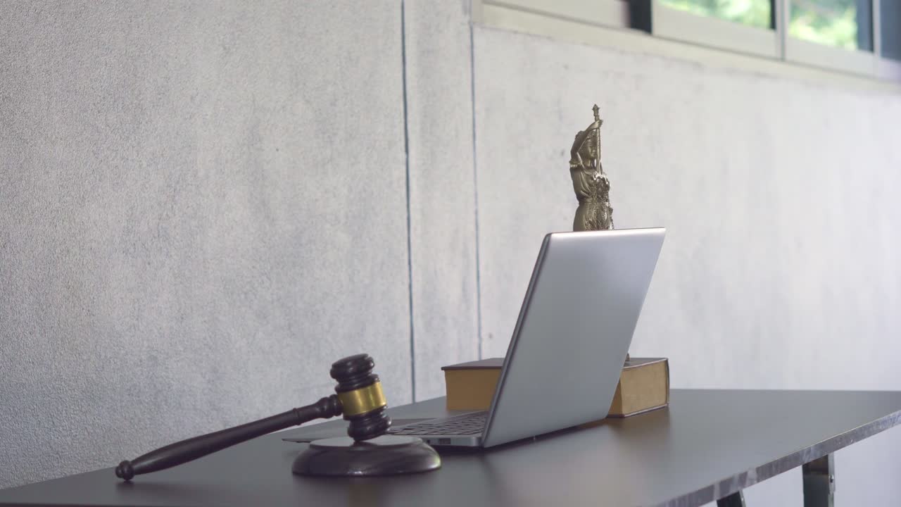 Laptop, martello del giudice, libri e bilancia. La dea della giustizia sul tavolo del concetto di consulenza legale.