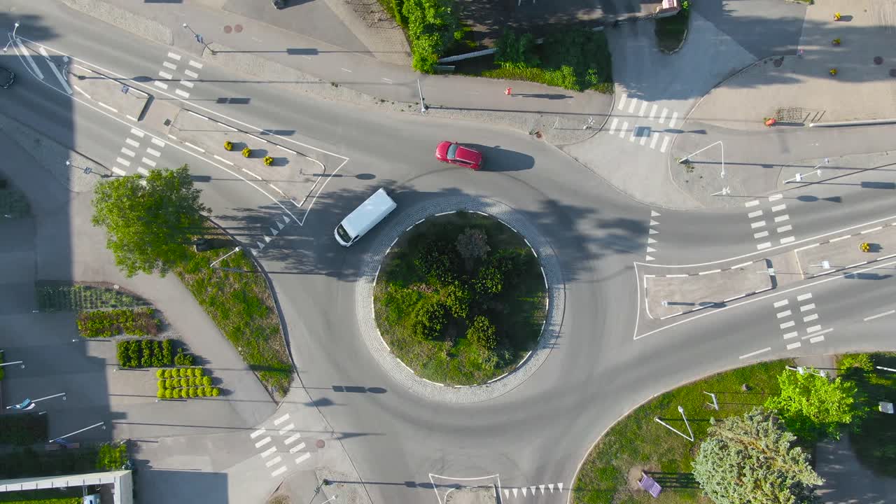 Aerial drone footage of a Roundabout in Laagri Estonia at Veskitammi. Camera moves up and starts spinning at the end showing traffic, with vehicles and cars driving and pedestrians and people walking.