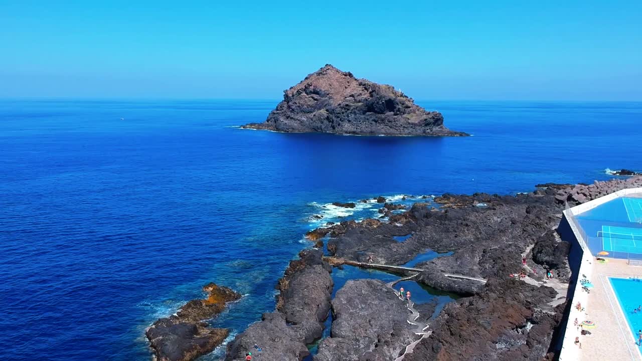 Aerial drone footage of the natural pools of Garachico Caletón. Blue ocean and the natural pools functioning as playas at Tenerife. Nice waves hit the rocks in the water.