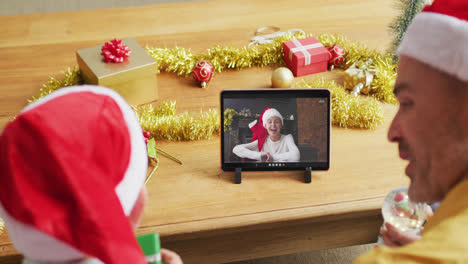 padre y hijo caucásicos con sombreros de santa usando una tableta para una videollamada de navidad con una mujer en la pantalla