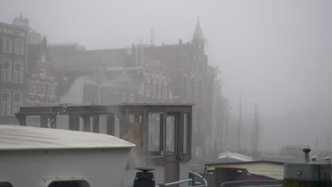 steam coming from the outlet of a hosueboat moored in a canal on a misty day in amsterdam