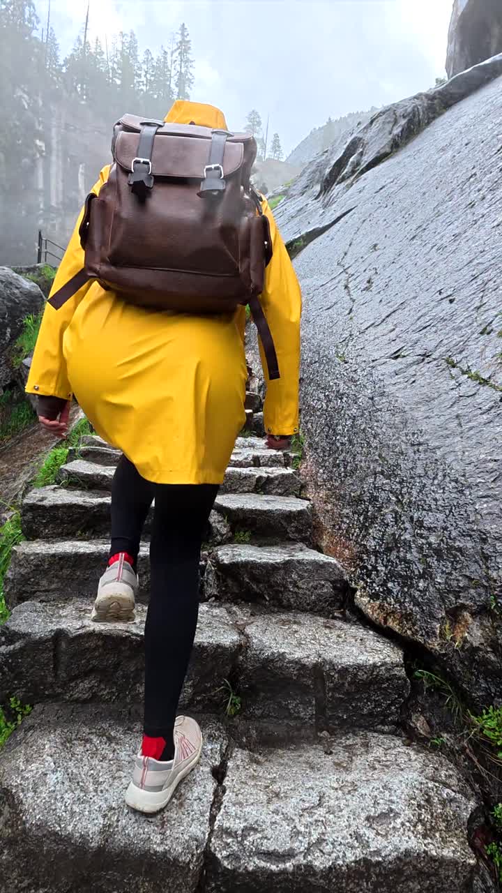 Persona con impermeabile giallo che sale gradini di pietra su un sentiero di montagna