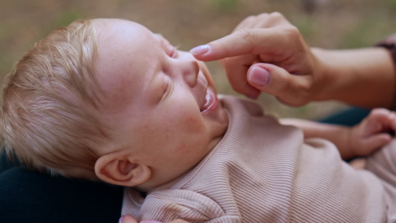 Mom's hand touches baby's nose and the kid smiles. Loving mother touching her child's face tenderly. Close up.