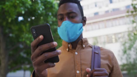 african american businessman wearing face mask using smartphone in street