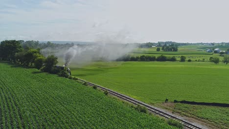 Una-Vista-Aérea-De-La-Campiña-De-Pensilvania-Con-Un-Solo-Motor-De-Vapor-Acercándose-Con-Humo-Y-Vapor-En-Una-Mañana-De-Verano