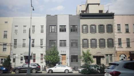 a colorful procession of cars passes before a row of multicolored brooklyn houses, others nestled neatly in parallel parking