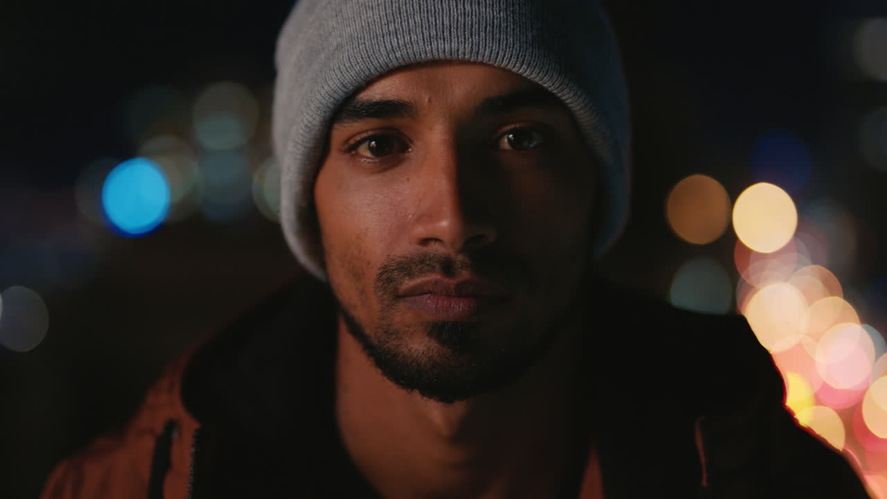 portrait of handsome young hispanic man on rooftop at night wearing beanie with bokeh city lights in urban skyline background