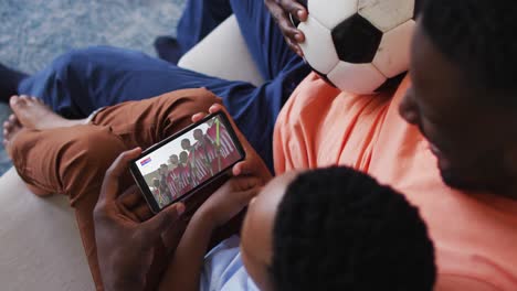 composite of father and son at home watching hockey match on smartphone