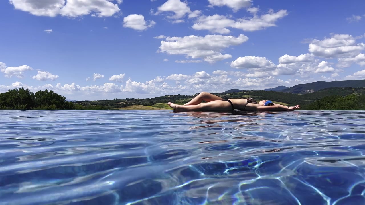 Woman relaxing on edge of infinity pool with countryside view