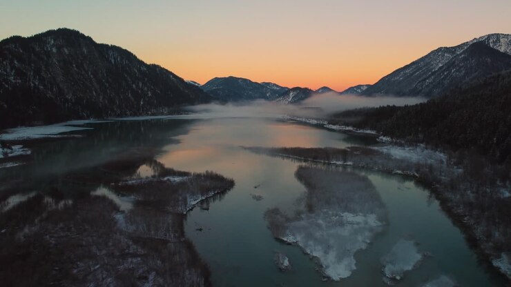 Beautiful Bavarian Austrian alps mountain river valley with fresh water at Sylvensteinspeicher by sunshine sunset, winter snow riverbed, trees and forest and mountains
