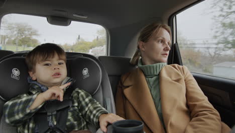 a woman with a two-year-old child is driving in the back seat of a car, a baby is sitting in a car seat