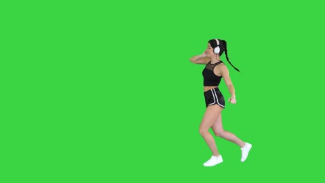 young happy sportive woman dancing and listening to music in headphones on a green screen, chroma key