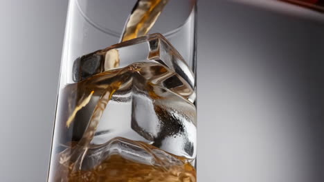 pouring a drink over ice cubes in a clear glass
